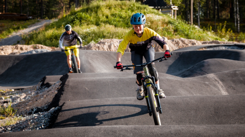 Kaksi pyöräilijää asfaltoidulla pumptrack-radalla.