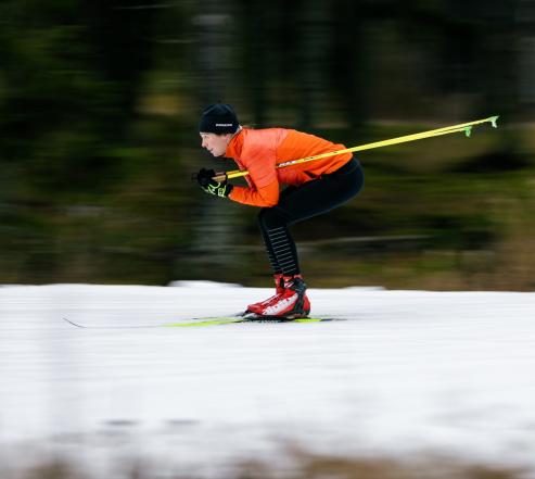 Hiihtäjä oranssissa takissa laskee mäkeä